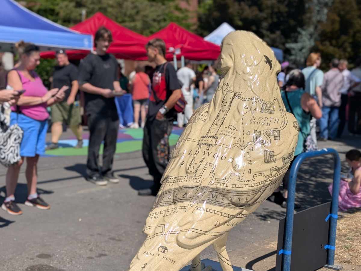 The back of a 5-foot crow sculpture with map of wildwood painted on a pale surface, crowd blurred in the background.