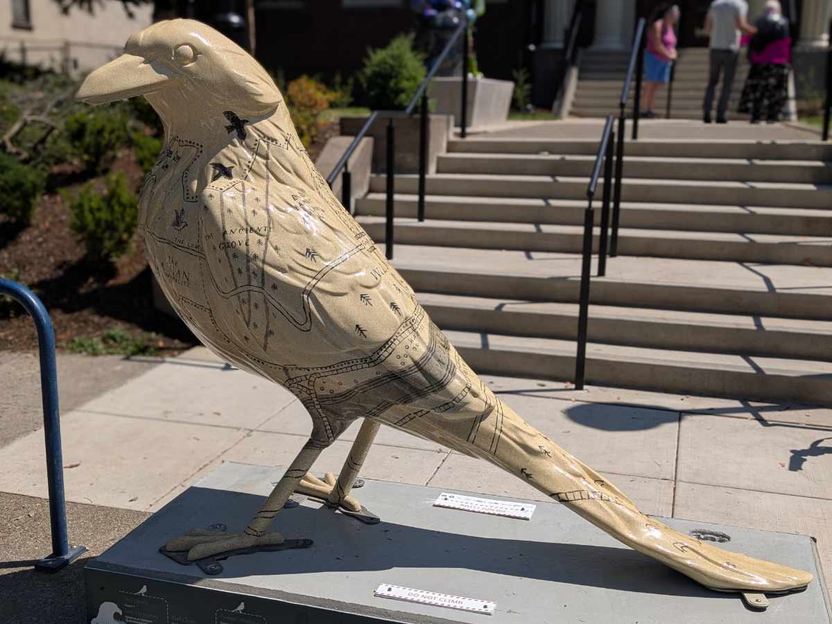 A statue along the Follow the Crows Trail in Portland, Oregon that is ecru in color and decorated with maps from the children's book Wildwood.